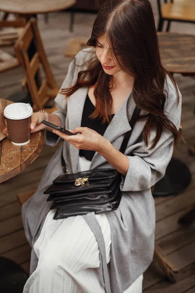 Hermosa Joven Mujer Sosteniendo Teléfono Sonriendo Con Taza Café Mesa —  Fotos de Stock
