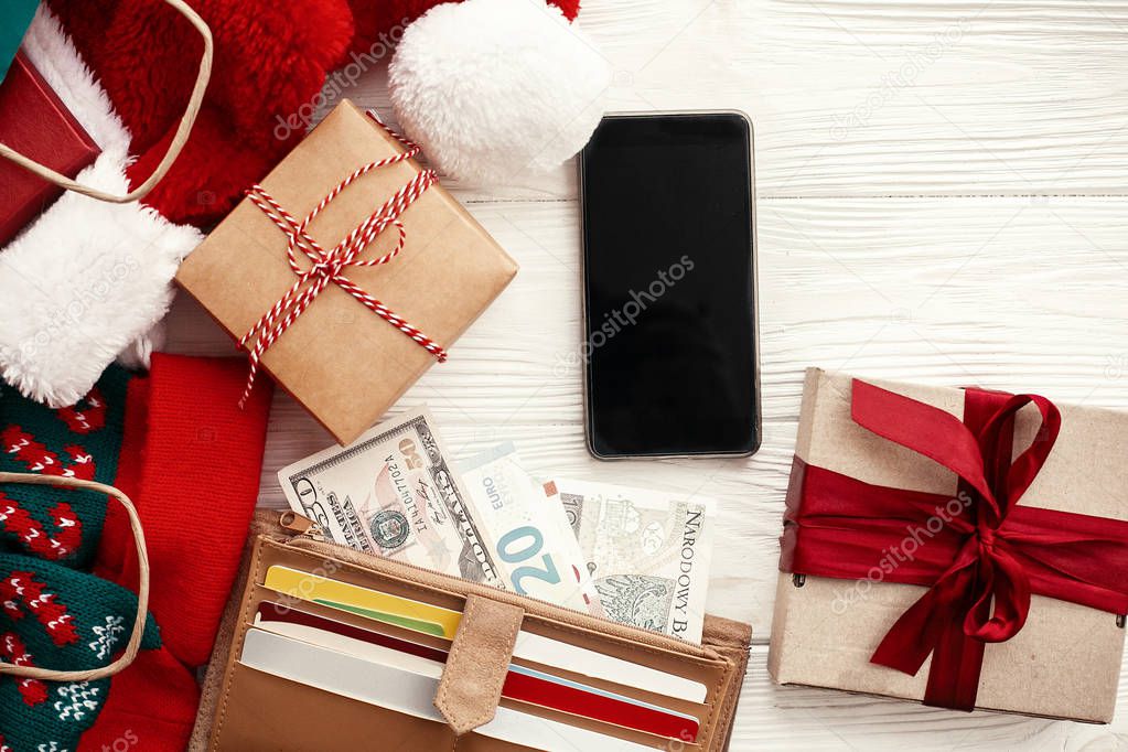 Credit cards and money in wallet, phone with empty screen, paper bags with clothes, gift boxes on rustic wood. Christmas shopping and seasonal sale. Advertising app.  Black Friday