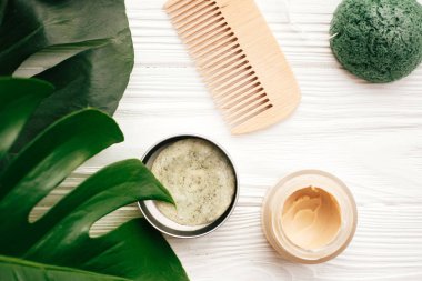 Doğal katı şampuan bar, ahşap fırça, saç kremi, sabun, yeşil monstera yaprakları ile beyaz ahşap üzerine konjaku sünger