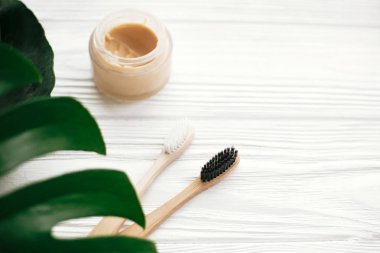 Doğal bambu diş fırçası ve diş macunu cam yeşil monstera yaprakları ile beyaz ahşap üzerine
