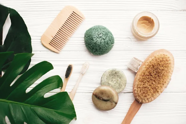 Natural solid shampoo bar, bamboo toothbrushes, wooden brush,  deodorant cream and konjaku sponge on white wood