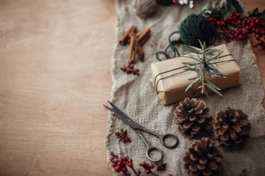 Yeşil dal ve çam dalları, kırmızı meyveler, çam kozalakları, rustik ahşap zemin üzerine tarçın ile şık rustik Noel hediye kutusu. Basit Eko dostu mevcut kaydırma. Atmosferik ruh hali