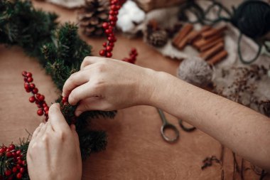 Rustik Noel çelenk. Çam dalları, kırmızı meyveler ve çam kozalakları, ip, holding eller makas, tarçın, rustik ahşap arka plan üzerinde pamuk. Tatil Atölyesi'nde atmosferik moody görüntü