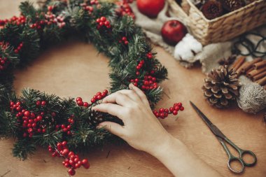 Rustik Noel çelenk ile çam dalları, kırmızı meyveler, çam kozalakları, ip, makas, tarçın, yapım eller rustik ahşap arka plan üzerinde pamuk. Tatil Atölyesi'nde atmosferik moody görüntü