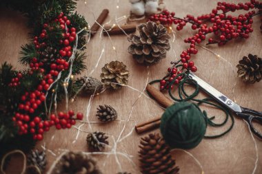 Rustik Noel çelenk. Çam dalları, çelenk, kırmızı meyveler, çam kozalakları, iplik, makas, tarçın, pamuk rustik ahşap zemin üzerinde. Noel çelenk, yapma