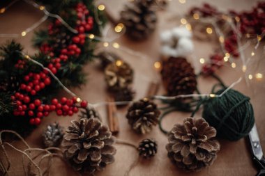 Çam kozalakları, çam dalları, çelenk, kırmızı meyveler, Tel, makas, tarçın, pamuk, rustik ahşap arka plan ışığı. Noel çelenk Atölyesi'nde yapmak için ayrıntılar. Atmosferik görüntü