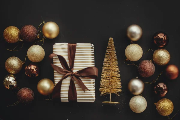 Noel şık hediye kutusu glitter ağaç ve modern siyah arka plan üzerine baubles ile düz yatıyordu. Modern kahverengi ve altın süslemeleri ve hediye. Mevsim selam. Mutlu Noeller