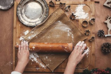 Hamur ahşap oklava ile gingerbread çerezleri için rustik masaya haddeleme eller. Üstten görünüm süreci hamur, eller, kesiciler, Noel süsleri ile pişirme. Atmosferik görüntü