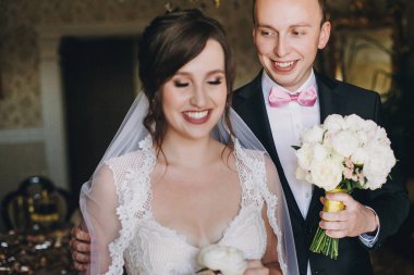 Şık damat yaka beyaz şakayık çiçeği elinde ile muhteşem elbise güzel gelini yürüyüş ve gülümseyen düğün buket ile. Güzel çift sabah hazırlanıyor