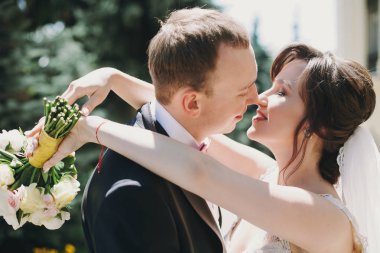 Muhteşem gelin şaşırtıcı elbise ve şık damat yavaşça güneşli parkta öpüşme. Vaktinizi ve açık havada kucaklayan güzel mutlu evlilik çift. Romantik duygusal an