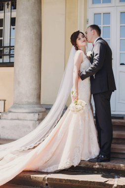 Şaşırtıcı elbise ve şık muhteşem gelin damat öpüşme ve eski binasında güneşli sokakta kucaklayan. Güzel mutlu evlilik çift yavaşça sarılma. Romantik duygusal an