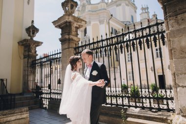 Şaşırtıcı elbise ve şık muhteşem gelin damat dans ve eski binasında güneşli sokakta kucaklayan. Güzel mutlu evlilik çift yavaşça sarılma. Romantik duygusal an