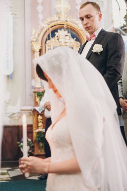 Damat gelini peçe altında mum ışığı ile dua ediyor iken bakarak. Mutlu şık düğün çifti kutsal evlilik bağıyla kilise sırasında mum tutan.