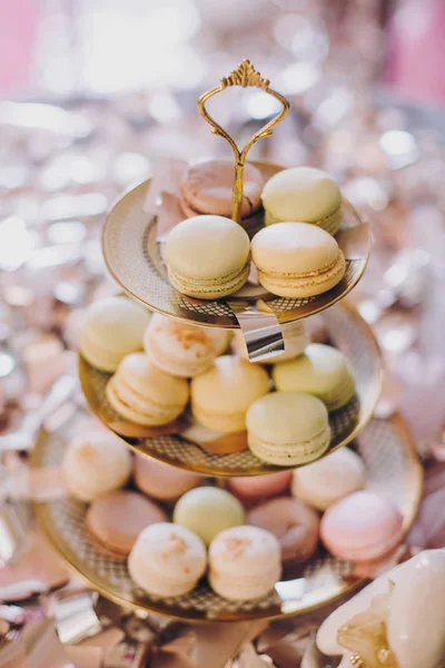 stock image Delicious colorful macarons on beautiful vintage stand with gold ornaments on table with gold and silver confetti. Luxury catering. Bridal hen or baby shower. French dessert macaroons