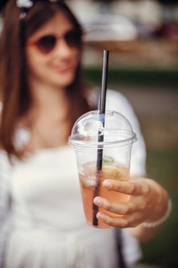 Tek Kişilik Kullanım plastik yasak. Plastik kap ve saman tutan mutlu hippi kız, retro elbiseli, güneş gözlüklü. Soğuk içecek tutarak ve şehir sokak rahatlatıcı güzel şık genç kadın.