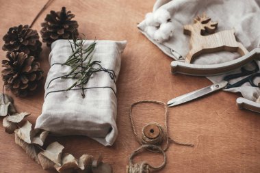 Şık Noel rustik Hediyelik yeşil çam kozalakları, Ren geyiği, makas, sicim, pamuk ile ahşap masa dalda ile keten kumaş sarılmış. Basit Eko plastik ücretsiz sunar. Sıfır atık tatil