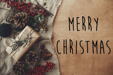 Neşeli Noel metin şık rustik Noel hediye kutusu ile çam dalları, kırmızı meyveler, çam kozalakları rustik ahşap üzerine oturum. Atmosferik görüntü. Mevsimlik tebrik kartı