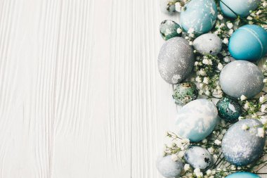 Metin, düz için yer beyaz ahşap zemin üzerine bahar çiçekleri ile şık Paskalya yumurtalarını bırakmak. Modern Paskalya yumurtaları mavi ve gri renkli doğal boya ile boyanmış. Mutlu Paskalya