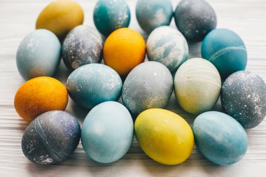 Beyaz ahşap zemin üzerinde şık Paskalya yumurtaları. Modern Paskalya yumurtaları mavi, gri, sarı mermer renkli doğal boya ile boyanmış. Mutlu Paskalya desen, tebrik kartı. Eko Tatil