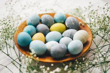 Bahar çiçekleri Beyaz ahşap zemin üzerinde ahşap plaka üzerinde şık Paskalya yumurta. Modern Paskalya yumurtaları mavi, gri, sarı mermer renkli doğal boya ile boyanmış. Mutlu Paskalya