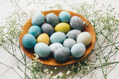 Mutlu Paskalyalar. Bahar çiçekleri Beyaz ahşap zemin üzerinde ahşap plaka üzerinde şık Paskalya yumurta. Modern Paskalya yumurtaları mavi, gri, sarı mermer renkli doğal boya ile boyanmış.