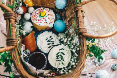 Paskalya sepeti ile yumurta, Paskalya ekmek, jambon, sosis, tereyağı ile çiçek ve rustik ahşap arka plan üzerine kumaş dallarda. Mutlu Paskalya kavramı. Dini gelenek, tatil gıda