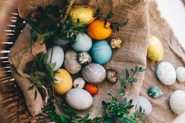 Beyaz ahşap arka plan, üstten görünüm üzerinde rustik sepeti şık Paskalya yumurtaları. Paskalya avı kavramı. Modern Paskalya yumurtaları doğal boya ve yeşil şimşir dalları ile boyalı. Mutlu Paskalya