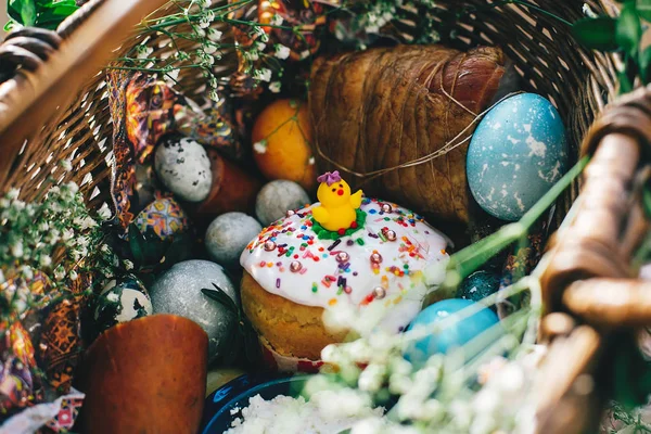 Easter basket with stylish eggs, easter bread with chicken, ham,sausage, and flowers with buxus branches  on rustic wooden background. Happy Easter concept. Traditional food