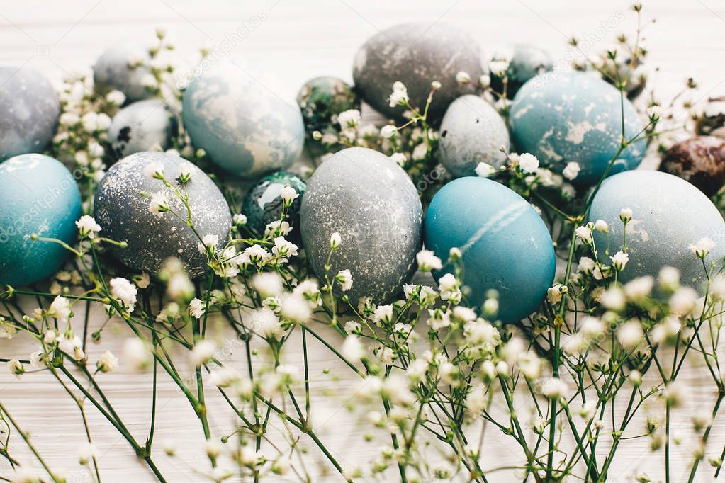 Stylish easter eggs with spring flowers on white wooden background. Modern easter eggs painted with natural dye in blue, grey  marble color. Happy Easter, greeting card