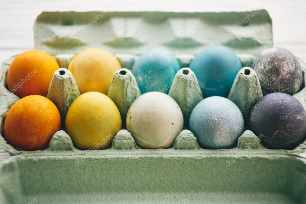 Stylish easter eggs in carton tray on white wooden background. Modern colorful easter eggs painted with natural dye in different colors. Happy Easter, eco concept