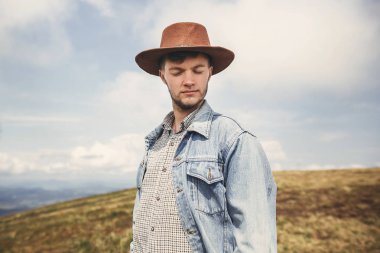 Şık hipster seyahat etmek üstünde tepe-in güneşli hills Dağları'nın arka plan üzerinde rahatlatıcı. Uzay kopyalayın. Yakışıklı adam dağlarında seyahat şapkalı. Yolculuk tutkusu kavramı.