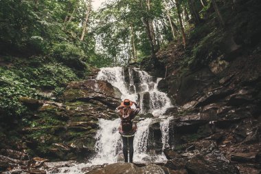 Genç kadın sırt çantası yaz ormanda keşfetmek ile şelale arıyorum. Seyahat ve yolculuk tutkusu kavramı. Metin için yer. Dağlarında seyahat şapkalı şık hippi kız.