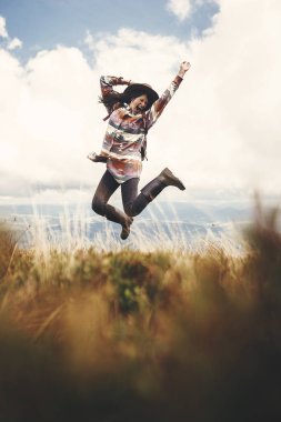 Şık hippi kız şapka ve dağlar üstüne atlama sırt çantası. Dağlarda eğleniyor mutlu genç kadın portresi. Seyahat ve yolculuk tutkusu kavramı. Muhteşem an