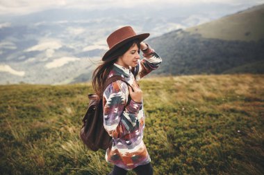 Seyahat ve yolculuk tutkusu kavramı. Dağlar üzerine yürüyen şapkalı şık hippi kız. Puslu Dağlar keşfetmek sırt çantası ile mutlu genç kadın. Muhteşem atmosferik an