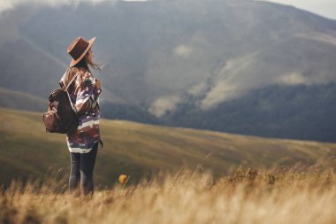 Dağlar üzerine yürüyen şapkalı şık hippi kız. Mutlu genç kadın güneşli dağlarda İnceleme sırt çantası ile. Seyahat ve yolculuk tutkusu kavramı. Muhteşem atmosferik an