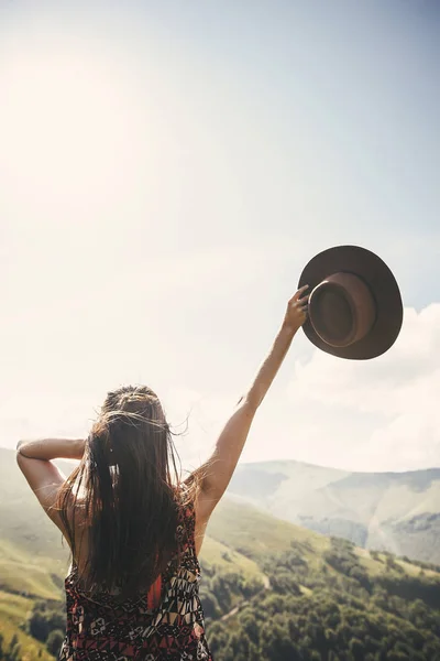 时尚的嬉皮士女孩戴帽子在阳光明媚的山顶上旅行 年轻美丽的女人与美丽的头发探索山和走在光明中 旅行和流浪欲望的概念 — 图库照片