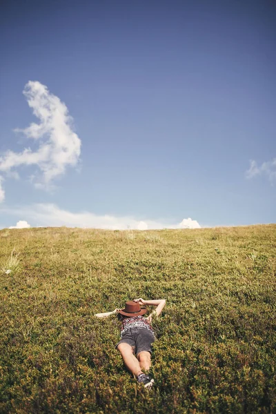 时尚的嬉皮士女孩在阳光明媚的山顶上放松的帽子 快乐的年轻女子躺在草地上 在夏天的山上休息 旅行和流浪欲望的概念 — 图库照片