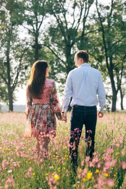 Elele ve pembe çiçekli bahar çayırda ışığında yürüyüş güzel genç bir çift. Güneş ışığı yeşil alanında gülümseyerek mutlu bir aile. Romantik anlar. Sevgililer günü