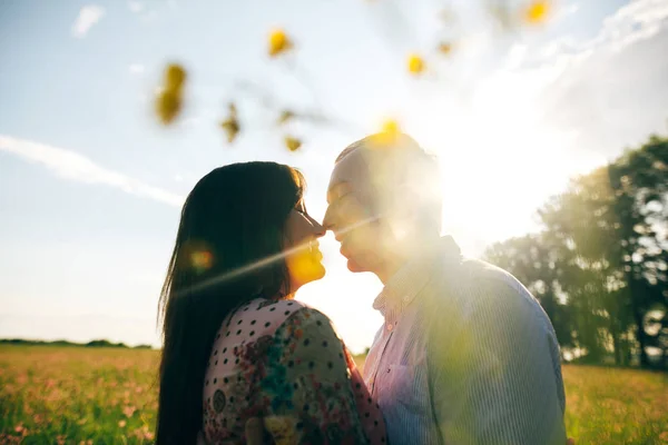 若くて美しいカップル優しくキスして 黄色の花の新鮮な春の牧草地の日差しの中でハグします 幸せな家族が日光の緑のフィールドを受け入れます ロマンチックな瞬間 花からの眺め — ストック写真