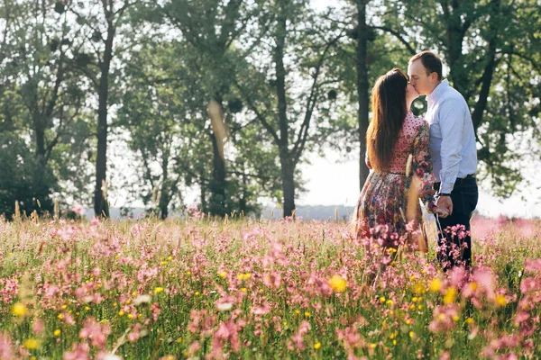 美しい若いカップルを手を繋いでいると ピンクの花で春の牧草地の日差しの中でキスします 幸せな家族が日光の緑のフィールドを受け入れます ロマンチックな瞬間 バレンタインの日 スペース — ストック写真