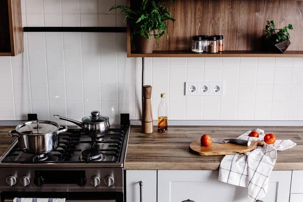 Cooking food on modern kitchen with steel oven, pots, knife on wooden cutting board with vegetables, pepper, spices,oil on wooden tabletop. Home food. Stylish kitchen furniture in grey color