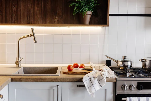 在现代厨房里用钢制烤箱 木制切菜板上的刀 木制桌面上的蔬菜在水水槽上做饭 家庭食品 时尚的灰色厨房家具 — 图库照片