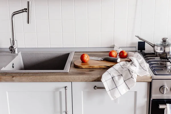 Cooking food on modern kitchen with steel oven, pots, knife on wooden cutting board with vegetables, spices on wooden tabletop at sink with water. Home food. Stylish kitchen furniture in grey color