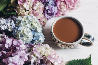 Güzel ortanca çiçek ve kahve fincanı rustik ahşap beyaz üzerinde. Renkli pembe, mavi, yeşil ortanca, tebrik kartı. Merhaba bahar. Mutlu anneler günü. Kadınlar günü. Günaydın kavramı