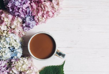 Güzel ortanca çiçek ve rustik ahşap beyaz kahve Kupası, düz yatıyordu. Pembe, mavi, yeşil renkli ortanca sınır, tebrik kartı ile metin için yer. Merhaba bahar. Mutlu anneler günü