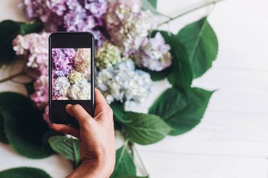El tutma telefon ve rustik ahşap beyaz ortanca çiçekleri alarak fotoğraf, düz yatıyordu. İçerik Sosyal medya kavramı, bloglama fotoğraflar için. Mutlu anneler günü. Dünya Kadınlar günü