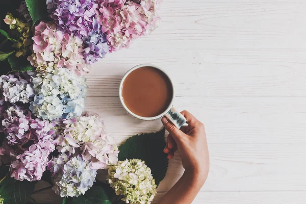 Handen Håller Kaffekoppen Vackra Hydrangea Blommor Rustika Vitt Trä Platt — Stockfoto