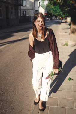 Modern takı güneşli street yürüyüş ile şık bohem kız. Boho mutlu hipster kaygısız kız bak çiçekli yaz şehir akşam rahatlatıcı. Metin için yer. Yaz tatili