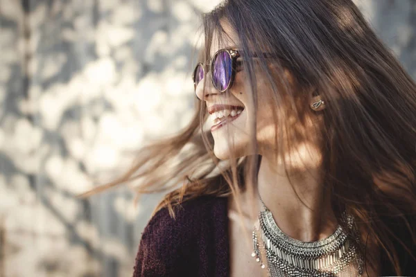 Mutlu boho kız güzel giysi ve güneşli sokakta gülümseyen güneş gözlüğü portresi. Şık hipster kaygısız kız ahşap duvar arka plan üzerinde poz. Metin için yer. Yaz tatil ve seyahat