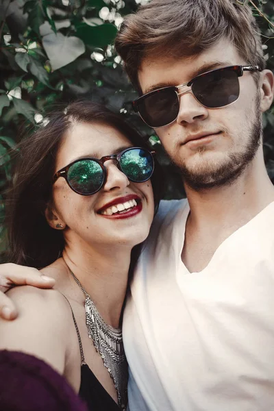 Stylish hipster couple in sunglasses smiling and making cool selfie. Happy family couple in love making self portrait and laughing in evening summer city. Vacation  and travel together